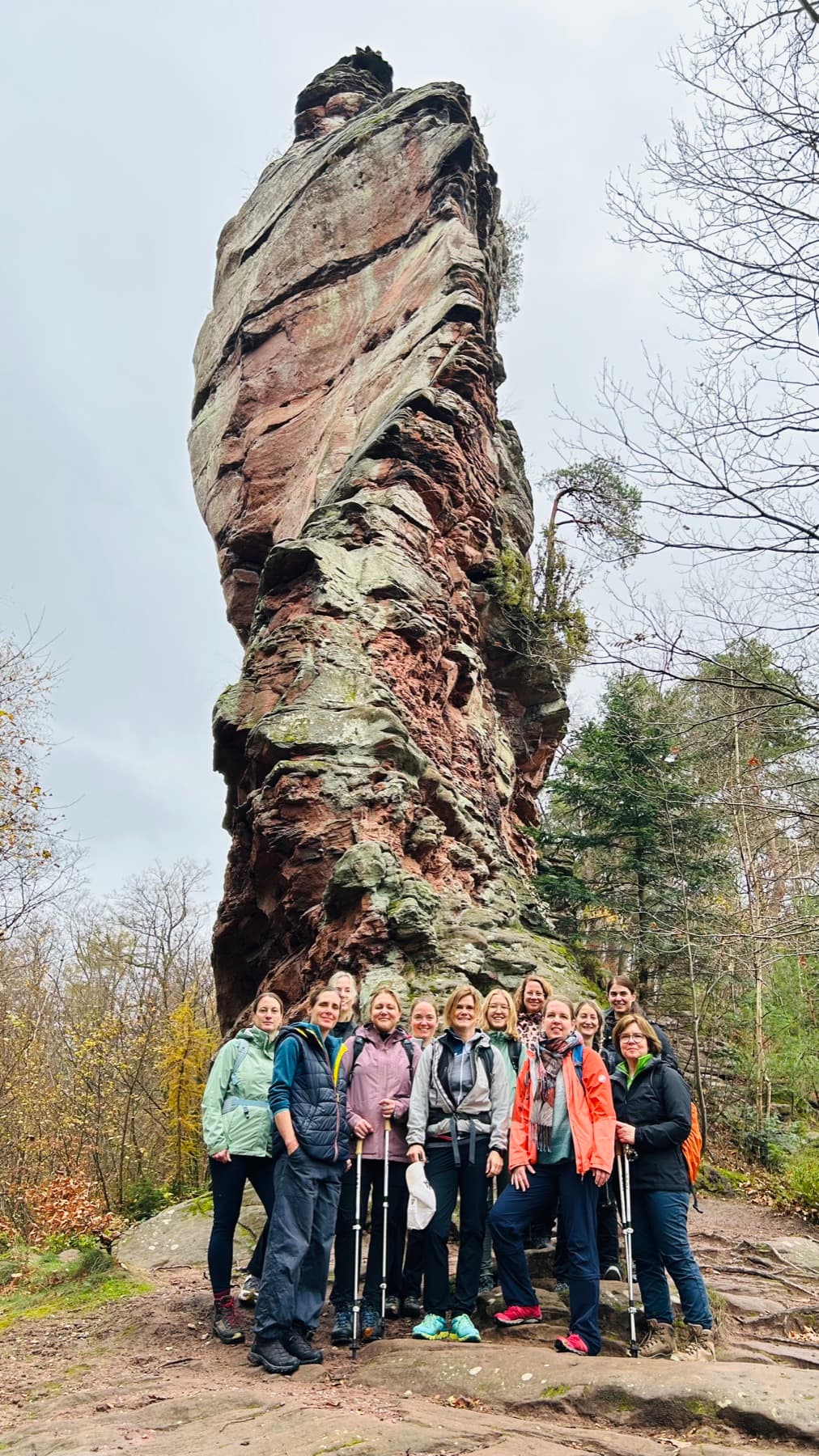 Wandergruppe vor einem hohen roten Sandsteinfelsen im herbstlichen Pfälzerwald
